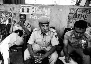 Black and White Photography with the title 'India 6'. Portrait of Indian Police Men sitting in front of a wall