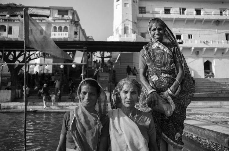 Schwarz-Weiss Fotografie mit dem Titel 'India 25'. Porträt von drei traditionell gekleideten Frauen, die auf einem Boot stehen.