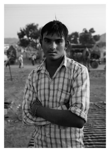 india 19 - black and white portrait of a young indian man facing the camera and standing with his arms crossed - by Will Falize - friendmade.fm