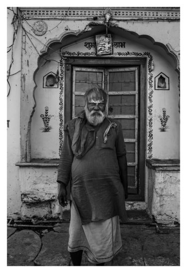 India 17 - black and white portrait of an indian man standing in front of a house - by Will Falize - friendmade.fm