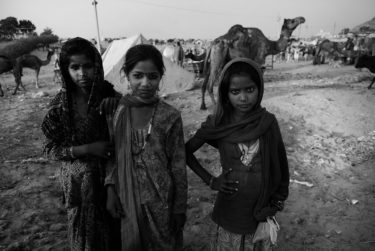 india 26 - black and white portrait of three indian girls in front of a camel - photographed by Will Falize - friendmade.fm